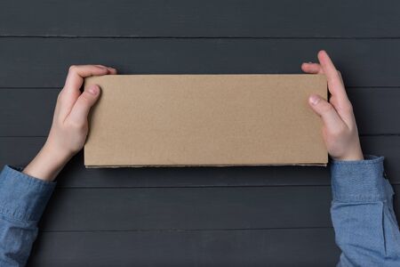Craft paper box in children's hands on black background. Top view. Copy space
