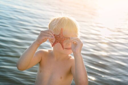 Funny fair-haired child playing with starfish. Seaside holiday with kids.の写真素材