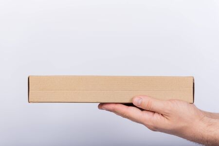 Flat cardboard box in male hands. Delivery of parcels. Side view