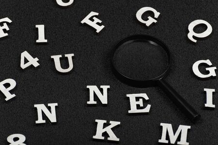 White letters and numbers and magnifying glass on black background. Search concept.