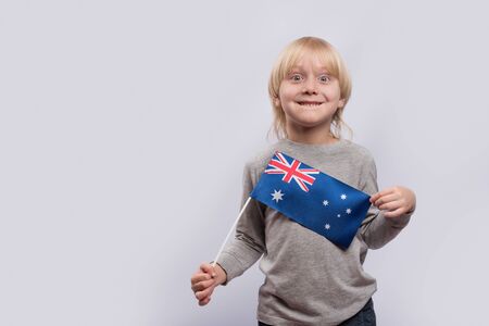 Portrait of cheerful blond boy with Australian flag in hand on white background.の写真素材