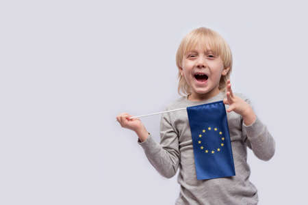 Smiling blond boy holding the EU flag in hand on white background. Trained in Europe concept.の写真素材