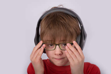 Boy in headphones corrects glasses. Portrait of child on white background close up.の写真素材