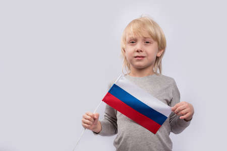 Portrait of cute blond boy with flag of Russia in hands on white background. Patriotism in Russia.