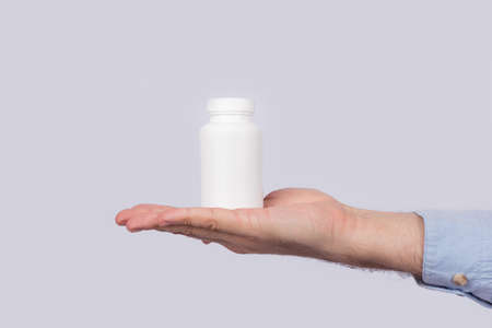 White plastic container for pills on palm on white background. Copy space. Template. Mockup.