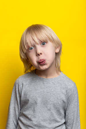 Funny fair-haired boy shows tongue and makes grimace. Vertical frame.の写真素材