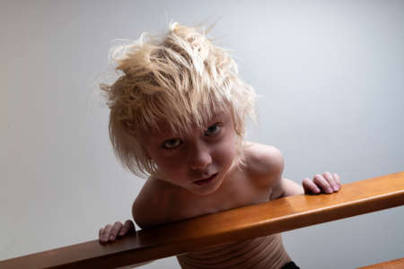 Child with blond hair leaned over the banister. Safety of child in houseの写真素材