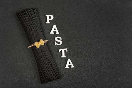 Raw uncooked black cuttlefish ink spaghetti and word Pasta on gray background