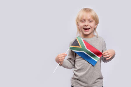 Cheerful smiling boy holding flag of South Africa on white background.の写真素材