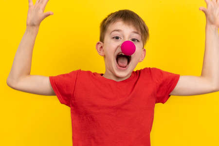 Happy boy with clown nose having fun on holiday. Portrait of child on yellow background.の写真素材