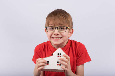 Scared little boy with glasses holds in hands of toy building. Childrens home shelter concept.