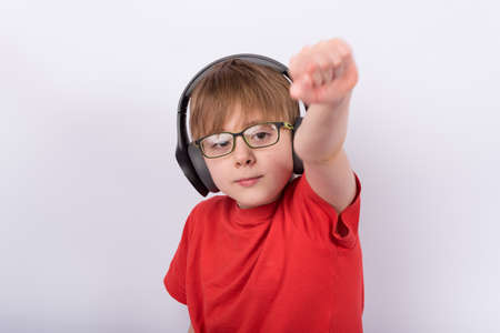 Portrait of boy like holding hand with fist up. Child with glasses and headphones on white background.の写真素材