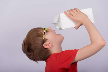 Boy drinking milk or juice from pack, white background. Copy space. Template. Mockup.
