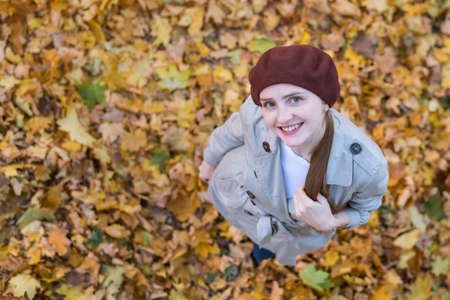Portrait of young beautiful woman in beret on autumn leaves background. Top viewの写真素材
