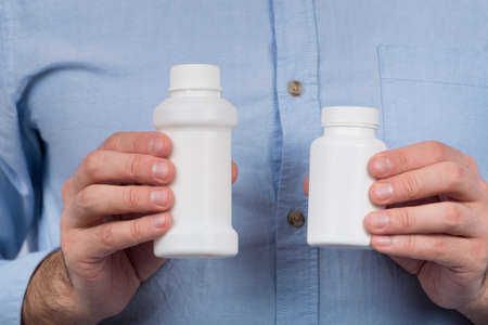Two white plastic bottles for medicines or vitamins in male hands. Copy space. mock up.