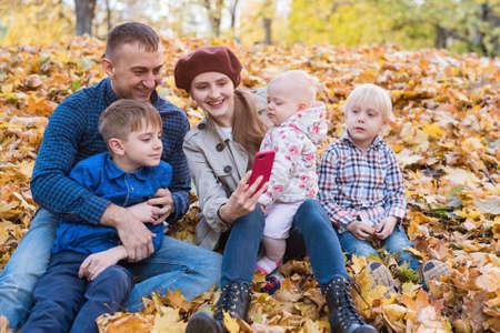 Large family sitting on fallen leaves in Park and make a selfie. Mum dad and three children.