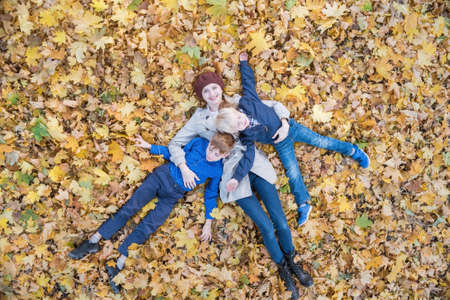 Mother and two sons lying on autumn foliage in forest. Young family in Park. Top viewの写真素材