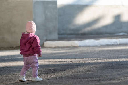 Small child stands alone on empty street. Girl in autumn clothes itself in the street. Safety of children.の写真素材