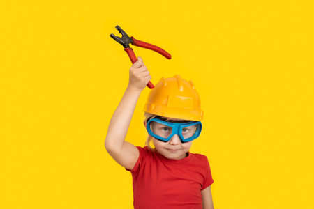 Child in construction helmet and goggles with holding pliers. Portrait on yellow background.の写真素材