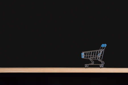 Shopping cart on black background. Trolley empty on wooden table. Side view. Copy space.の写真素材