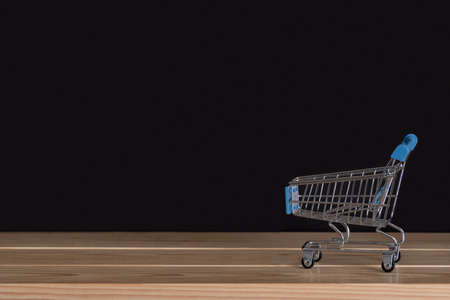 Empty shopping trolley on wooden table. Black background. Copy space.