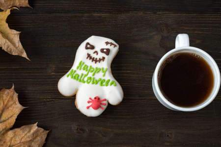 Gingerbread with words Happy Halloween and Cup of tea. Wooden background beside autumn leavesの写真素材