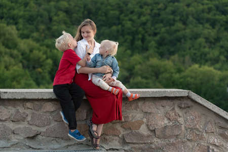 Mom and two children are sitting against nature background. Portrait of mother with children on vacationの写真素材