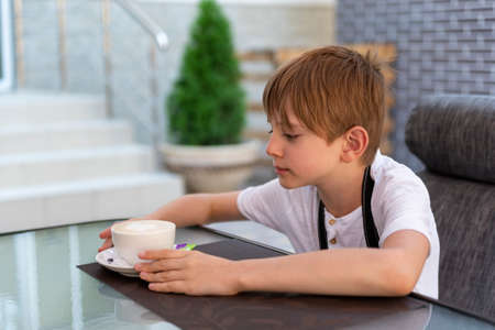 boy is drinking coffee in cafe. Child in restaurant. independent teenager.の写真素材
