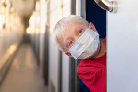 Blond boy in protective mask rides train compartment. Traveling during a quarantine. Empty train.の写真素材