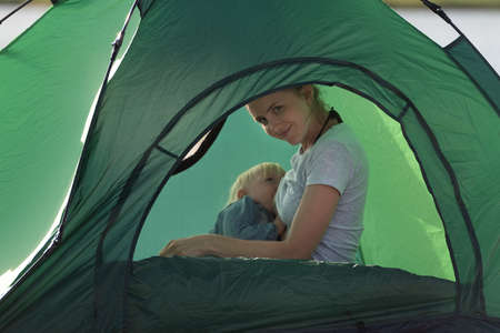Mom is breastfeeding her baby in camping tent. Camping with children.の写真素材