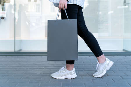 Black shopping bag in female hand, legs on background. Space for text. Sale or Black friday.の写真素材