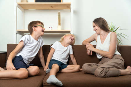 Mother and two sons are sitting on couch and have fun talking. Family friendly relations.