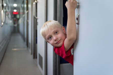 Blond boy in train carriage looks out of compartment. Traveling with children by trainの写真素材