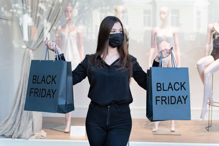 Woman in black and medical mask holds shopping bags with Black Friday inscription