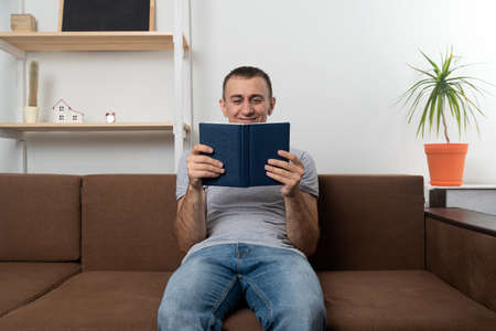 Guy is sitting on couch and reading book. Home education.