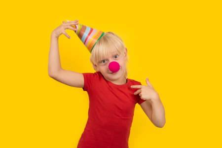 Little 5 years blond boy wearing party cap and red clown nose. birthday partyの写真素材