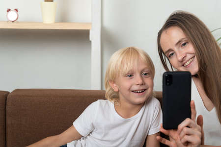 Young mother and son look into smartphone and smile. Selfie on phone.