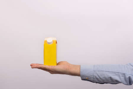 Blank yellow cardboard bag with cap on mens palm. Packet of juice or milk. mock up.の写真素材