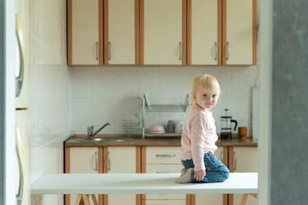 Little blonde girl sitting on the table in kitchen. Awaiting breakfast.の写真素材