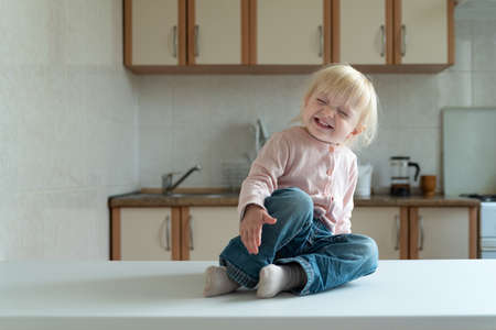 Little blonde girl sits in the kitchen and laughing. Happy child.の写真素材