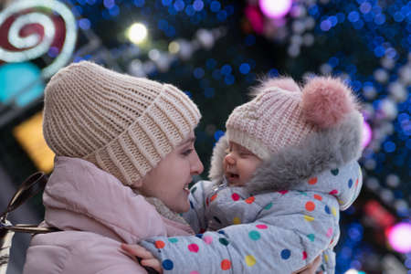Portrait of mom and daughter in warm hats against New Year's tinsel backgroundの写真素材