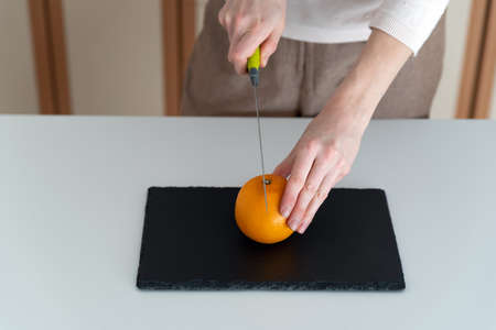 Female hands cut orange on black cutting board. kitchen tools.の写真素材