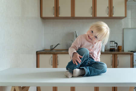 Little blonde girl sits in the kitchen and smiles slyly.の写真素材