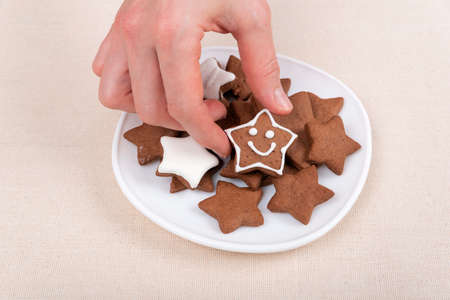 Female hand holds a gingerbread cookie in shape of star emoticon. Glazed painted cookies.の写真素材