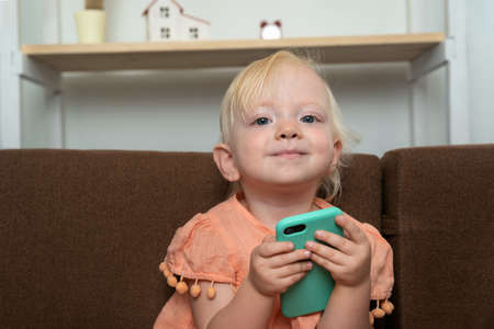 Baby is holding phone in her hands and smiling. Portrait of child with smartphone in his hands.