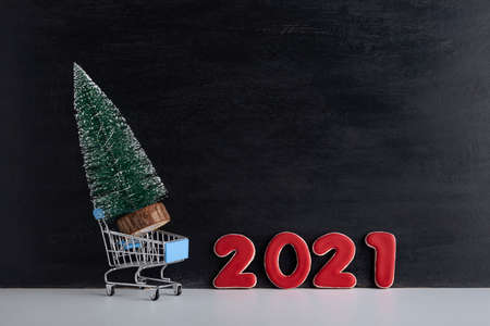 Miniature Christmas tree in trolley cart against the background of inscription 2021. Purchase and...