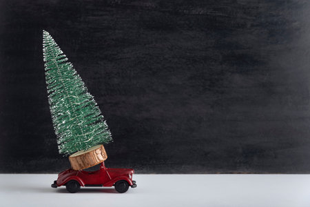 Toy car carries miniature Christmas tree. Delivery of Christmas trees concept. Copy spaceの写真素材