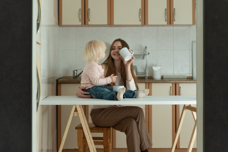 Mother and daughter in kitchen. Happy young mom and toddler have breakfast at homeの写真素材