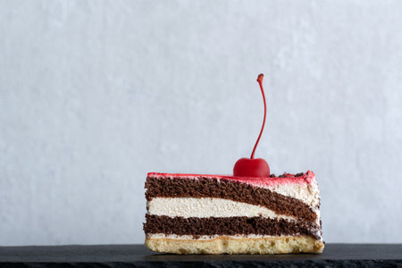 Piece of chocolate cake garnished with cherry. Side view to piece of cake. White background.