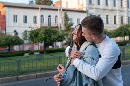 Guy hugs girls shoulders and kisses her. Young couple in love hugging outdoors.の写真素材